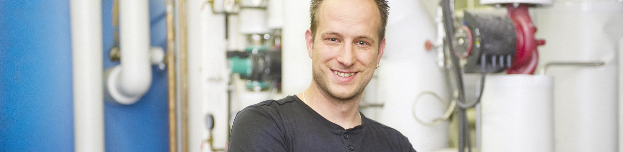 Mann mit verschränkten Armen lächelnd vor Rohrleitungen und Ventilen